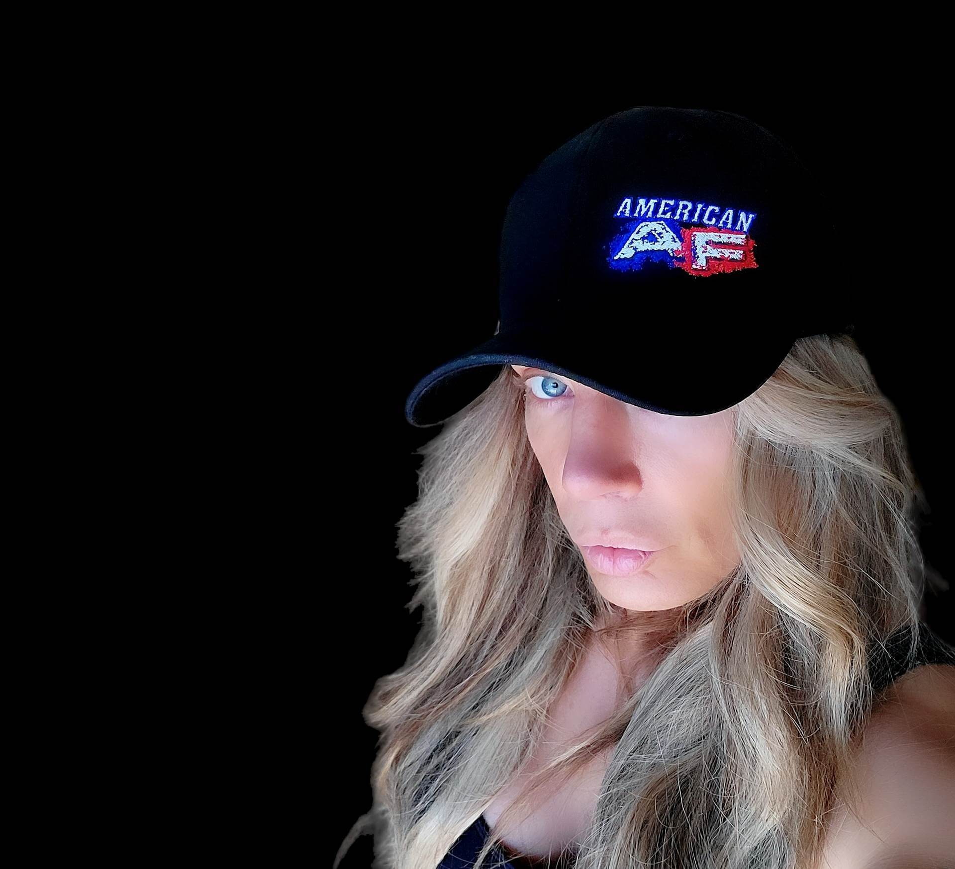 American AF flexfit hat worn by a person with long blonde hair in front of a black background.