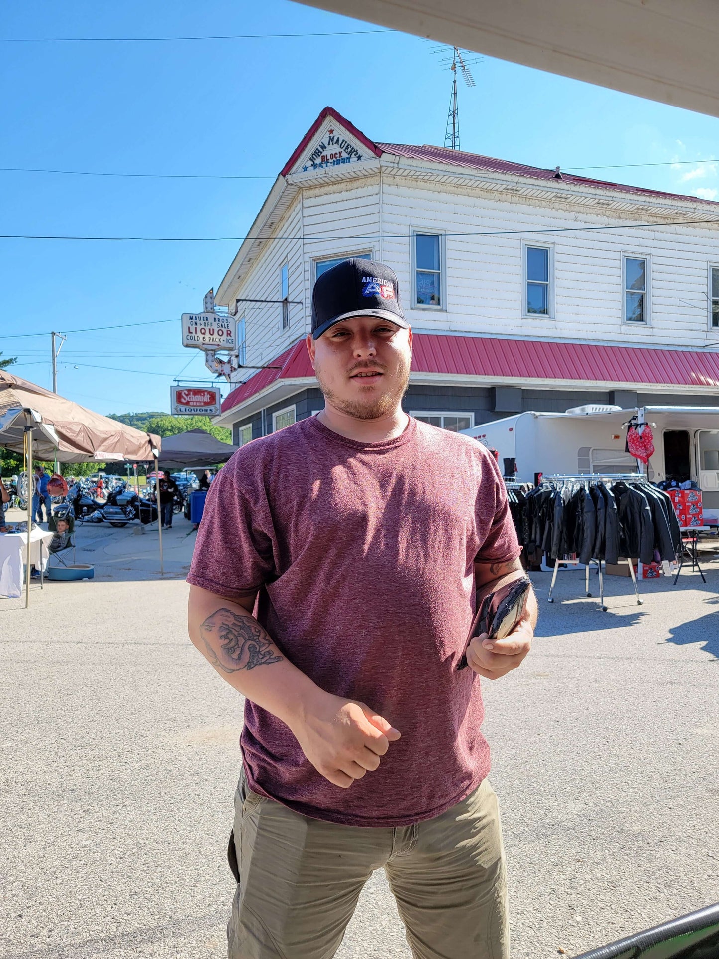 Man wearing an American AF flexfit hat and maroon shirt, with a street market background.
