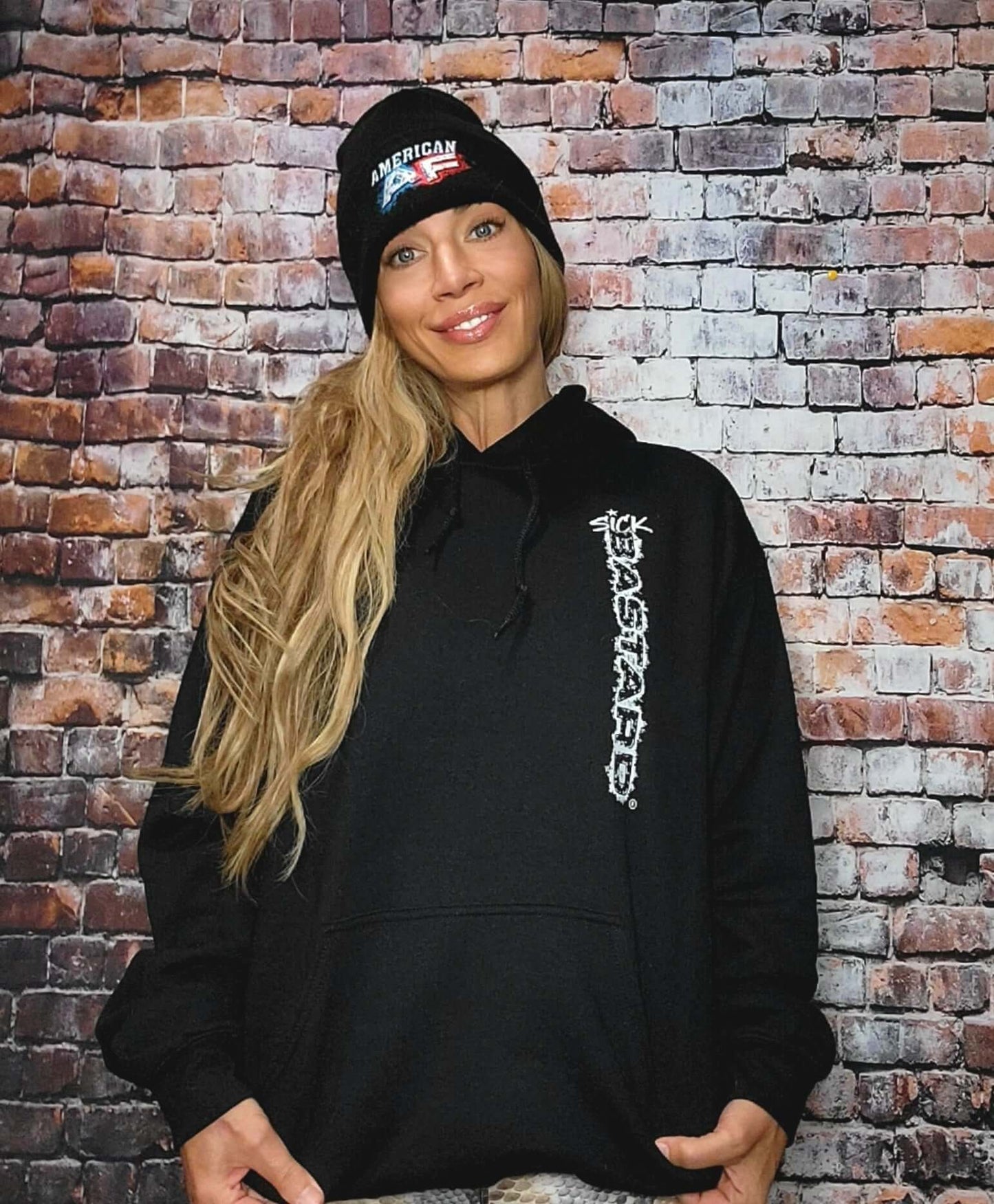 Model wearing a black fucked up hoodie from Sick Bastard Streetwear against a brick wall.