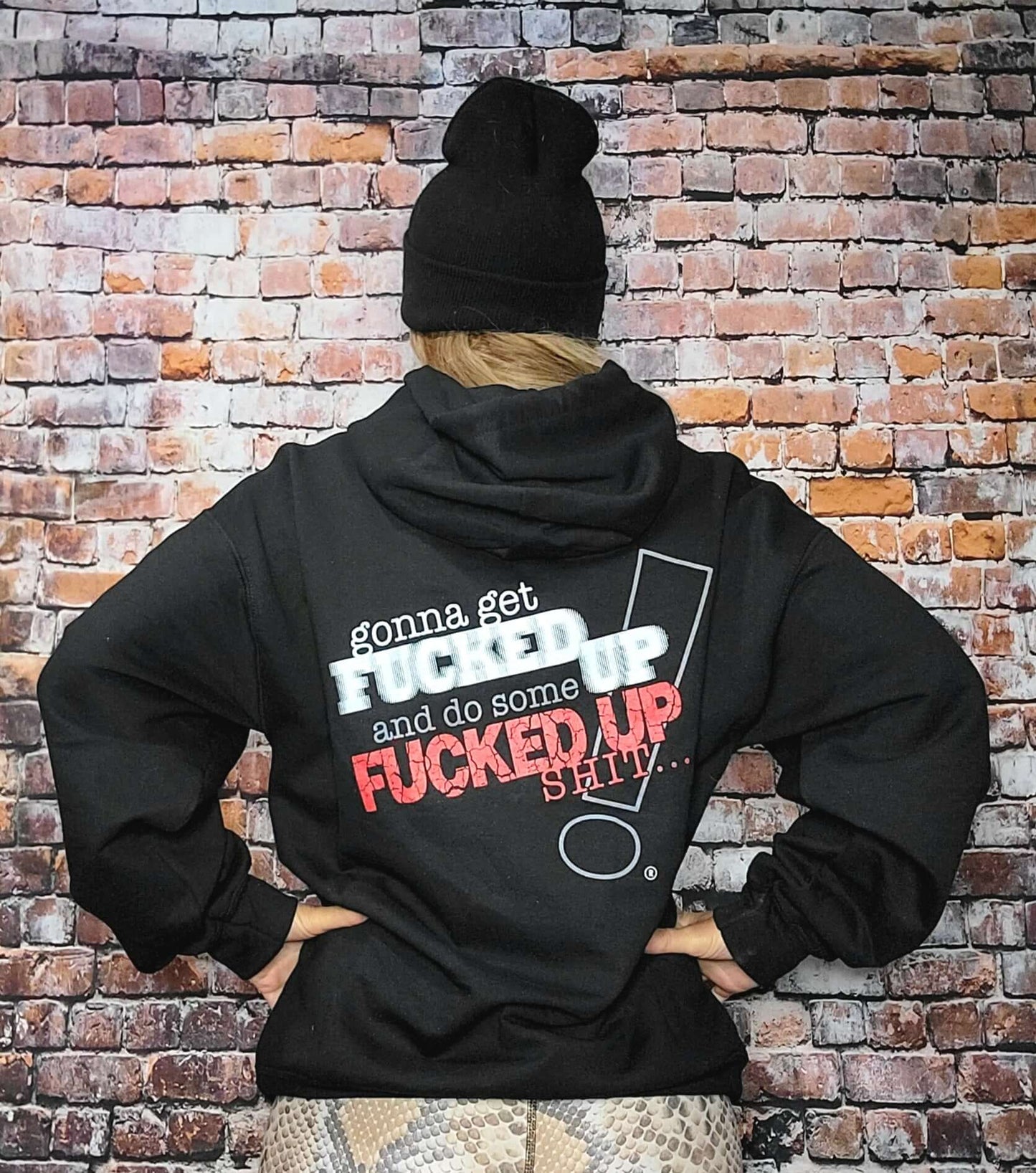 Back view of person wearing a Fucked Up hoodie with bold text on a brick background.