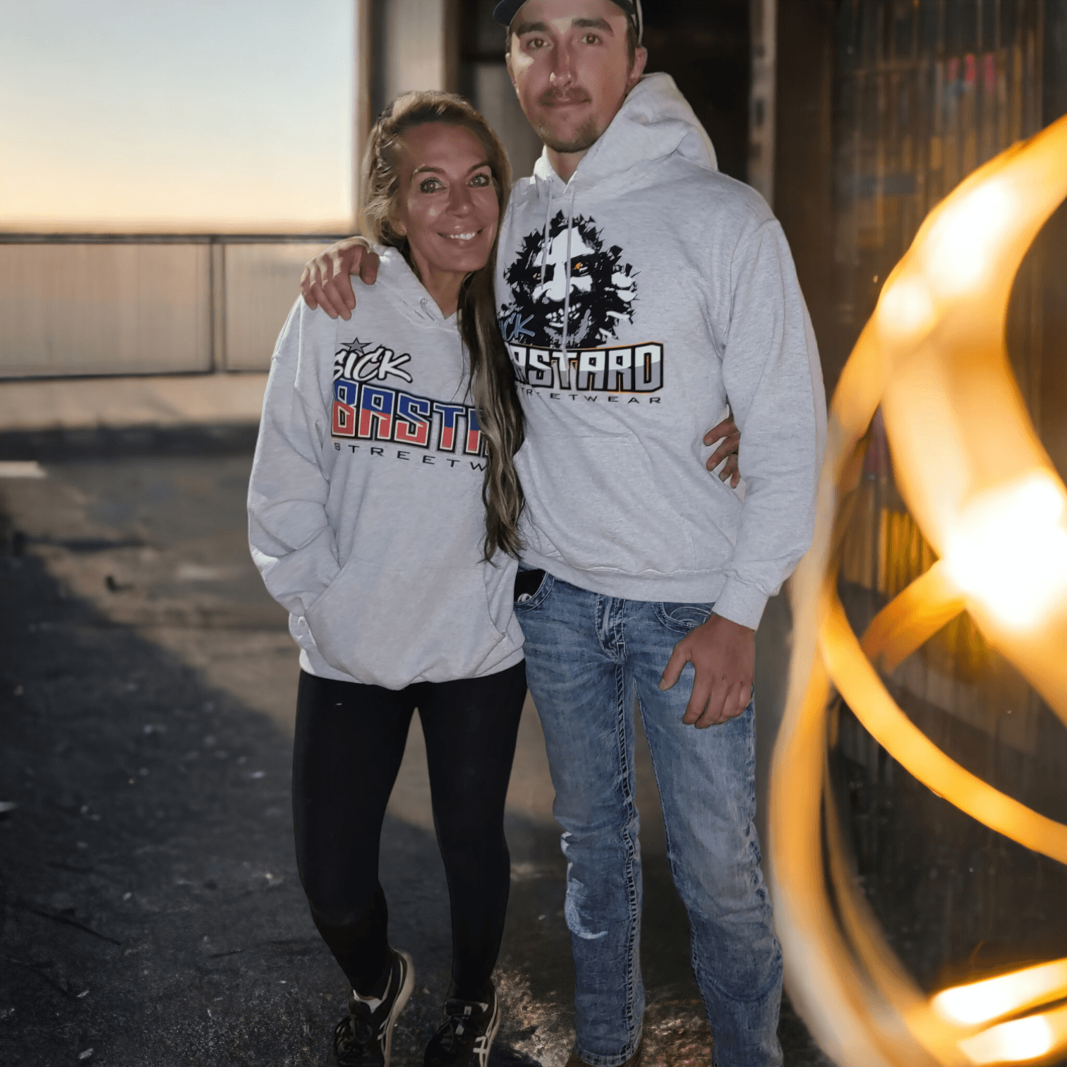 Couple wearing cheap pullover hoodies featuring Sick Bastard logos outdoors.