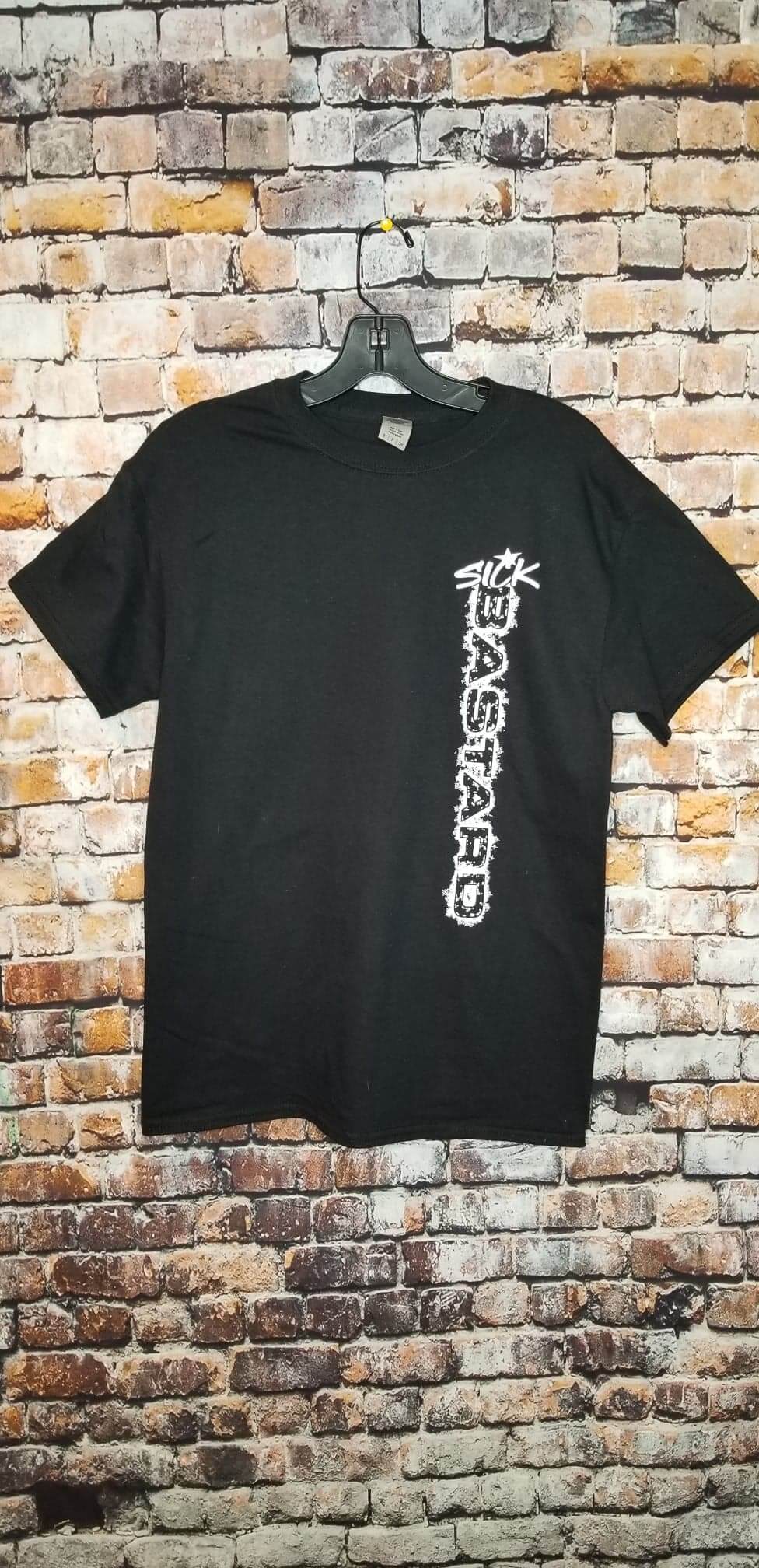 Funny graphic t-shirt displayed on a hanger against a brick wall, showcasing bold white writing.